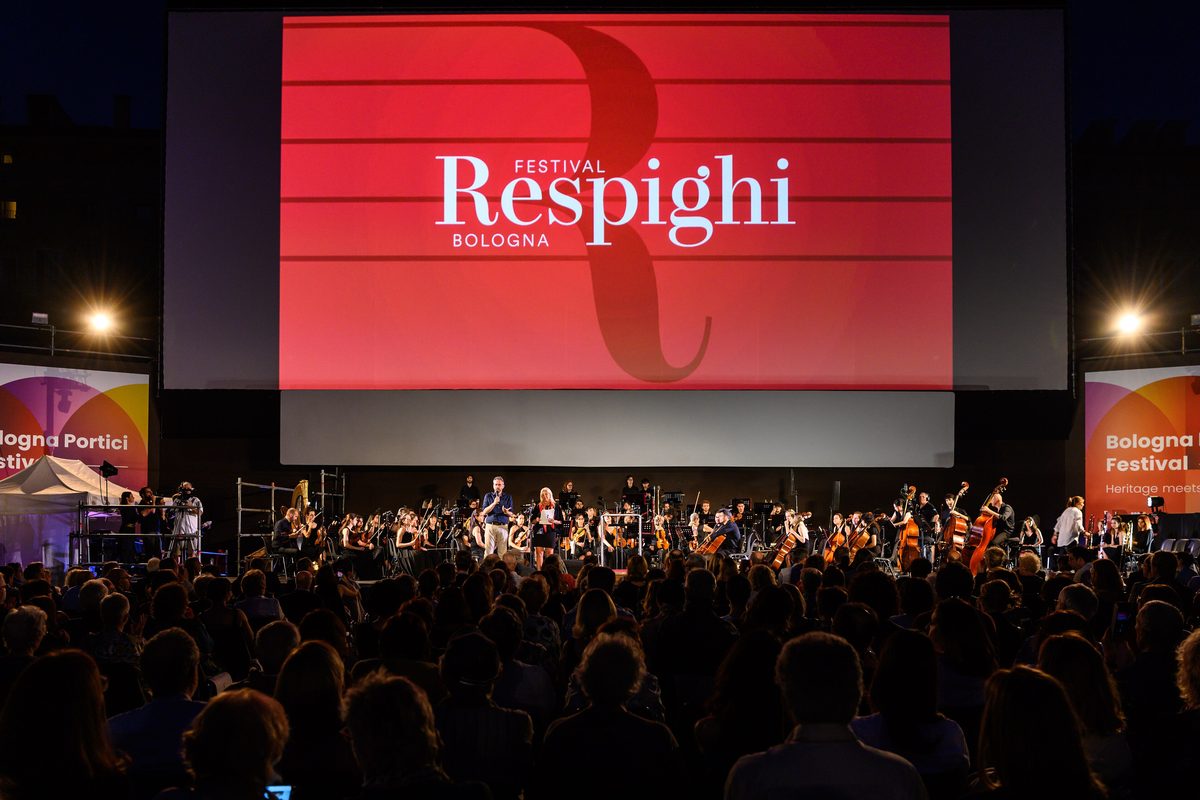 An orchestra on an open-air stage in Piazza Maggiore, Bologna, in front of a large audience