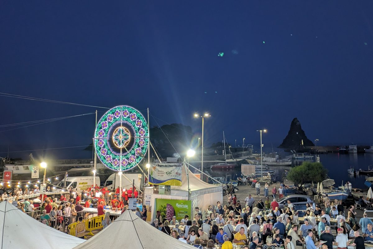 Crowds and festival tents by the sea at night at the Sagra del pesce spada in Aci Trezza, Sicily