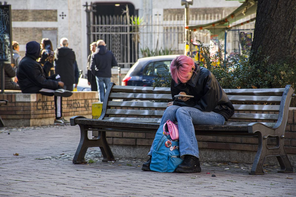 A person on a bench in an Italian square looking at a phone