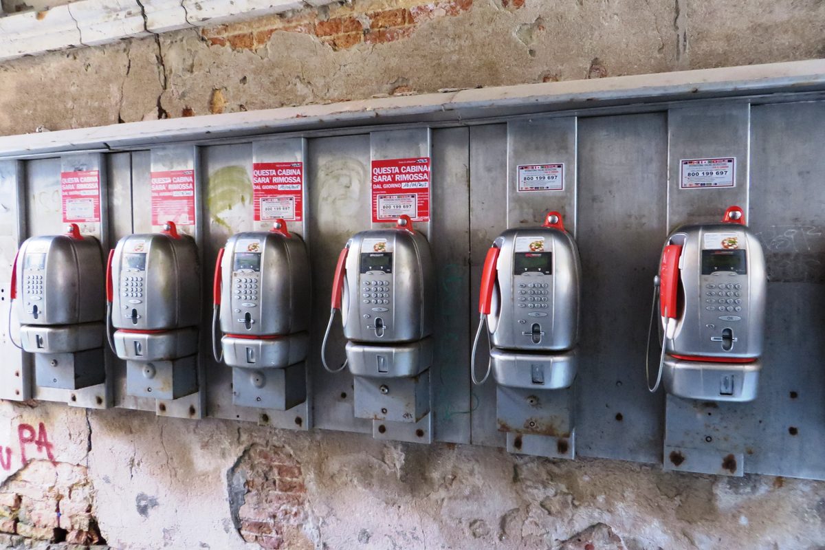 A row of old public telephones on a brick wall in Italy