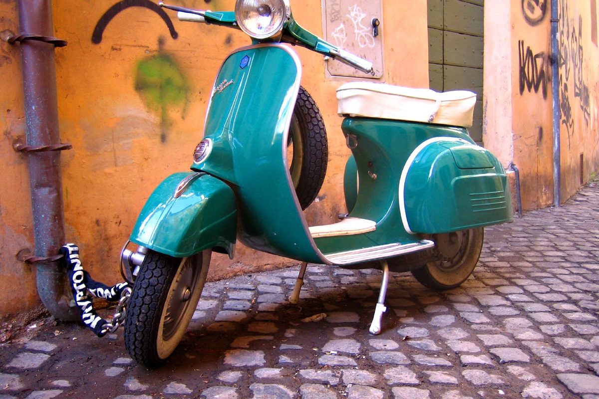 A turquoise Vespa parked on a cobbled street in Rome