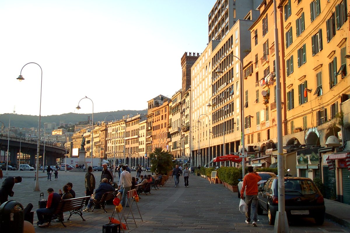People walking and sitting in Piazza Caricamento in Genoa at sunset