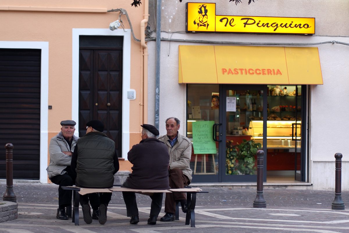 Four elderly men chatting on a bench in front of a pastry shop in Sant'Antioco, Sardinia