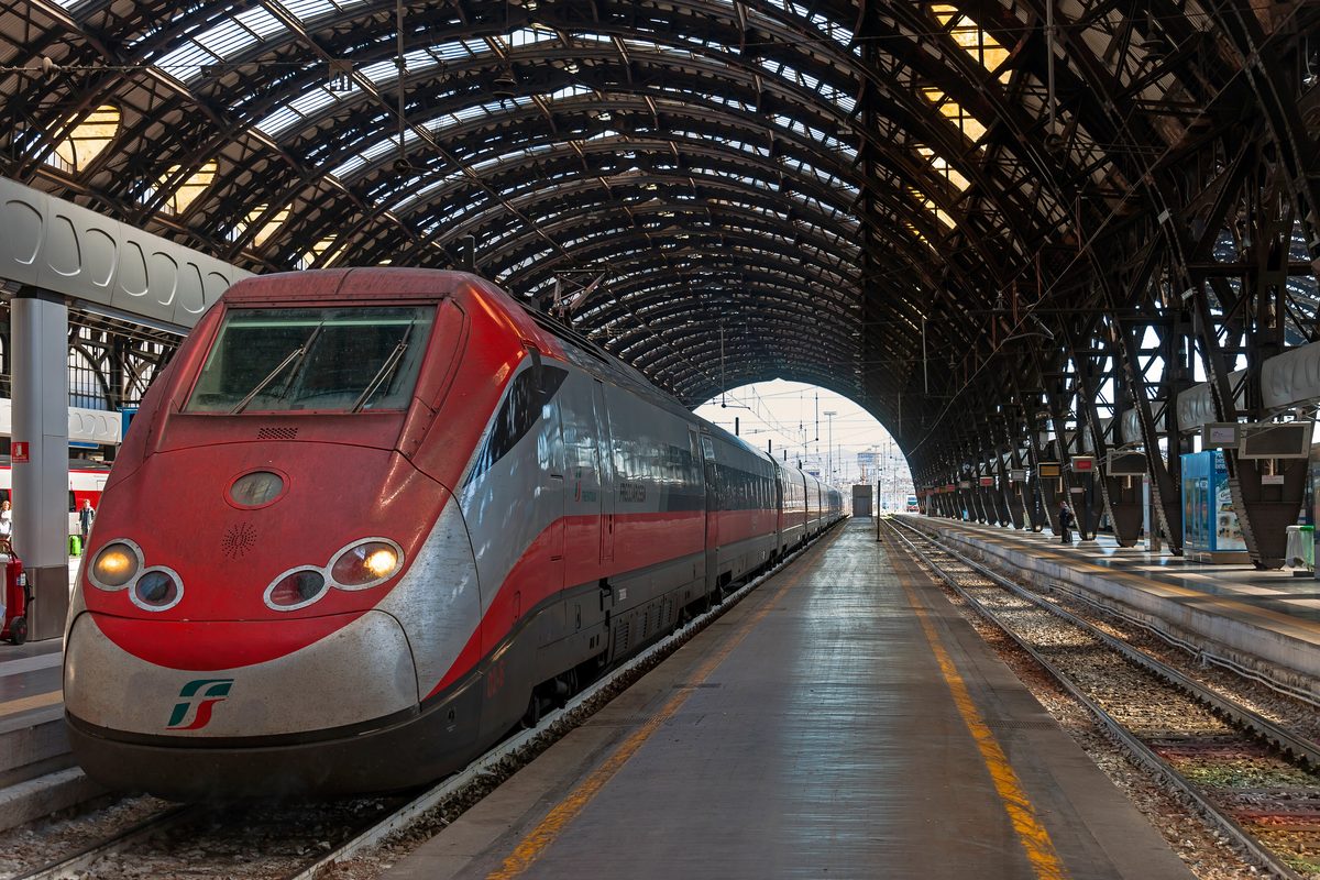 A red Frecciarossa high-speed train at a platform under the iron roof of Milano Centrale