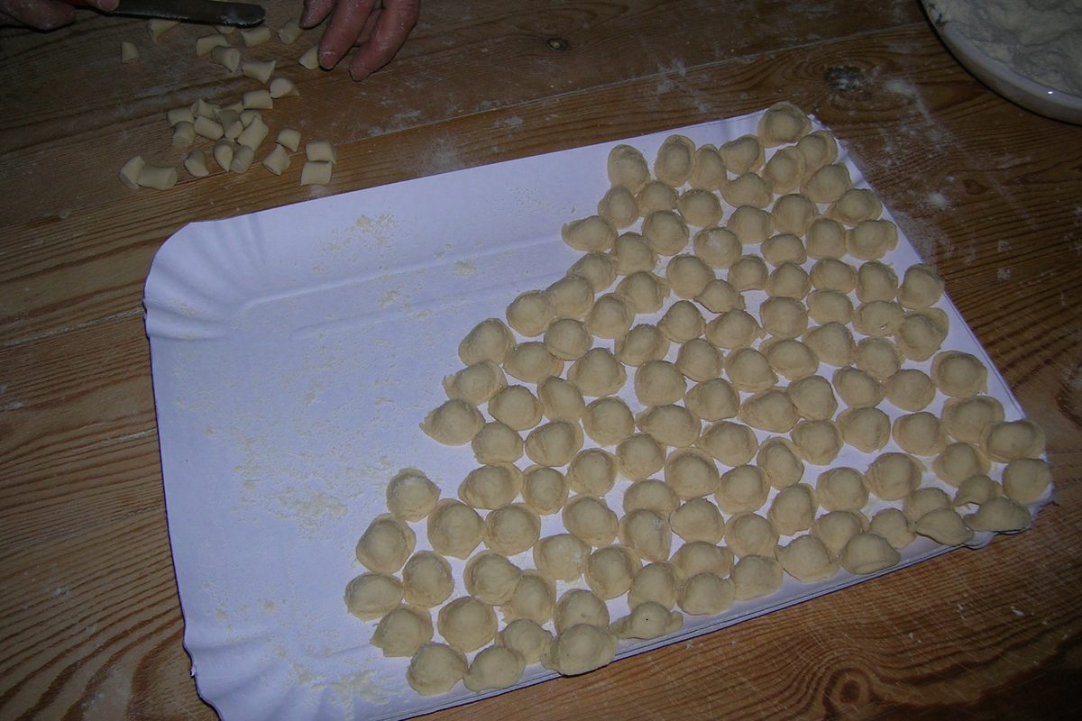 Small hand-made orecchiette laid out on a paper tray, with the knife used to shape them