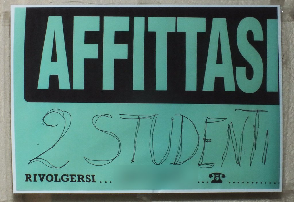 Een bordje “Affittasi” (te huur) aan de muur, met “2 studenti” met de hand geschreven